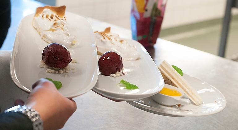 Närbild på tre fat med desserter som bärs fram av en servitris.