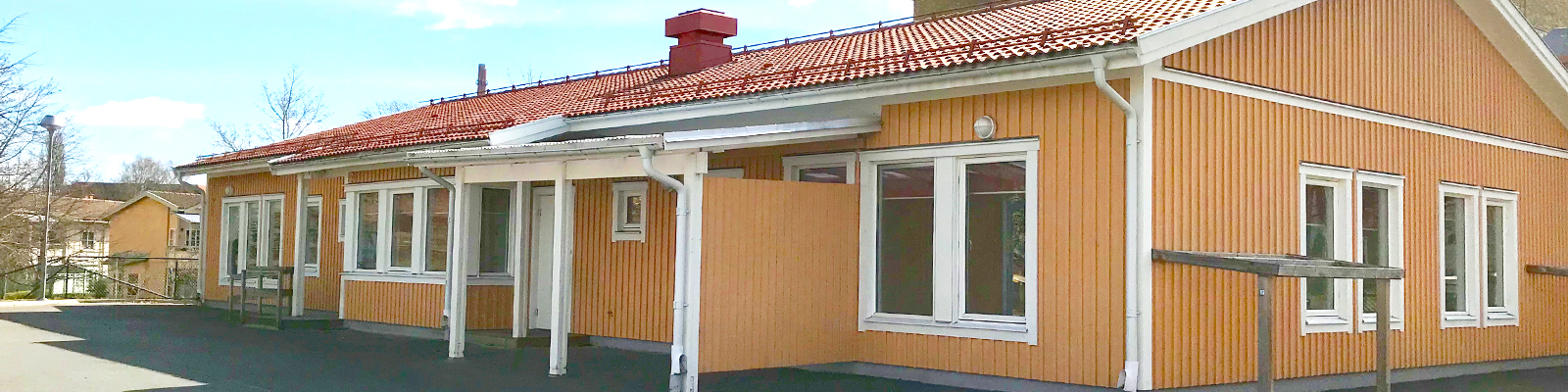 Ett lågt gult trähus med vita knutar i solsken.