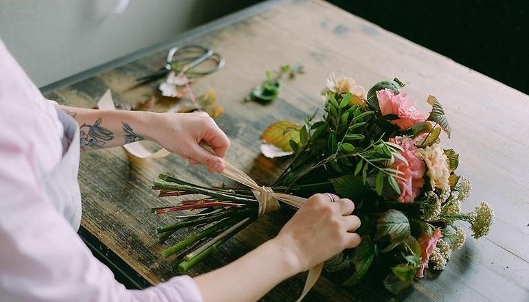 En person knyter en rosett runt en bukett med rosor och andra blommor.