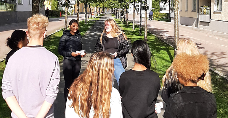 Två tjejer är guidar runt en grupp ungdomar i stadsmiljö.